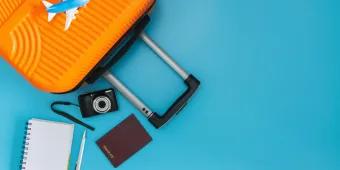Travelling to the US An orange suitcase, toy plane, passport, camera and notepad on a blue background