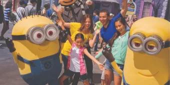 A joyful family with two young kids raising their hands in excitement while meeting the Minions and Gru at Universal Studios Florida, highlighting an essential Universal Orlando Resort experience.
