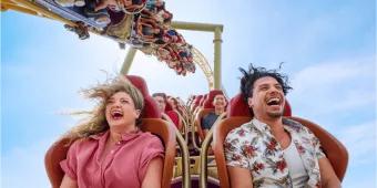 Two adults laughing and screaming with their hair flying while riding a high-speed roller coaster at Universal Orlando Resort, illustrating the kind of thrill ride experience you secure by booking tickets in advance.