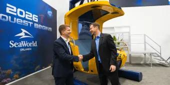 Two men shaking hands in front of the ride vehicle, a yellow hanging seat.