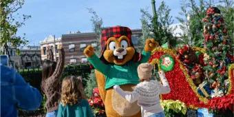 Children waving at a friendly squirrel character, surrounded by Christmas decorations and red poinsettias, capturing a joyful holiday season moment and a memorable experience in Orlando.