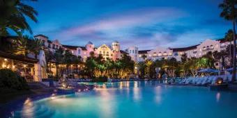 Illuminated lagoon-style swimming pool and tropical architecture at a premium Universal Orlando Resort hotel at night.