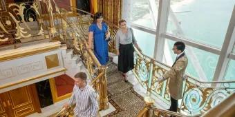 Guests on the Burj Al Arab Inside Tour walking down the luxurious gold staircase with an attendant, showcasing the opulent interior and expansive ocean view.