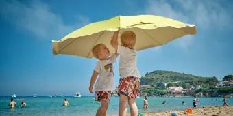 Children playing with beach umbrella on family summer vacation.