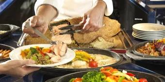 A chef serving fresh salt-crusted salmon and roasted vegetables at a Disneyland Paris buffet.
