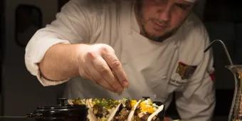 A chef garnishing fresh gourmet tacos on a platter at a Universal Orlando Resort restaurant.