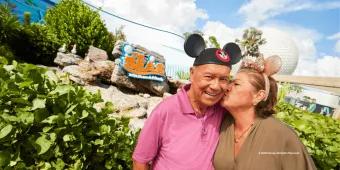 Couple wearing Mickey and Minnie ears near The Seas with Nemo & Friends pavilion at EPCOT, with Spaceship Earth in the background