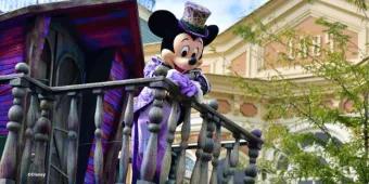 Mickey Mouse in a purple Halloween costume and top hat waving from a balcony at the Disney Halloween Festival