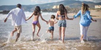 Family enjoying a summer beach holiday in Europe, running into the ocean together