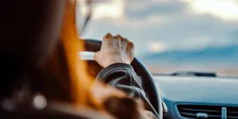 Over-the-shoulder view of a person holding a steering wheel while driving