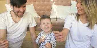 A young family celebrating together at home with sparklers, smiling and laughing