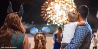 A family wearing Disney ears looking out at a nighttime fireworks display
