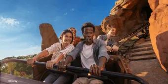 A group of smiling guests holding onto the lap bar while riding Big Thunder Mountain