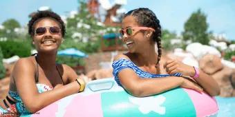 Two smiling women floating together on a colorful inflatable inner tube in a water park pool
