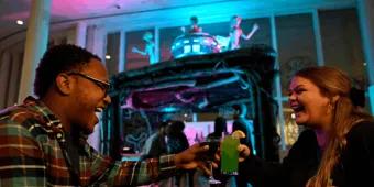 Two guests laughing and clinking colorful themed cocktails at a Universal Orlando Resort hotel Halloween Horror Nights bar experience