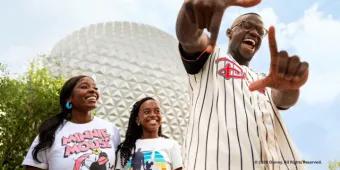 Family smiling in front of Spaceship Earth while a man makes a frame with his hands