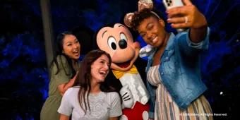 Two guests taking a selfie with Mickey Mouse at night