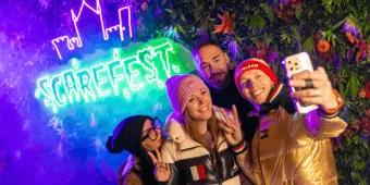 Four friends taking a selfie in front of a glowing neon Scarefest sign