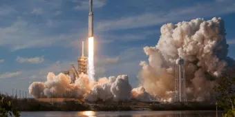 A SpaceX Falcon Heavy rocket launching from the pad, surrounded by large plumes of exhaust