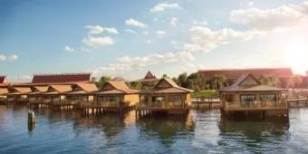 Luxurious bungalows at Disney's Polynesian Village Resort built over water, sitting underneath a sunny blue sky