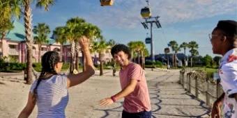 Friends standing on the beach of Disney’s Caribbean Beach Resort, laughing underneath the Skyliner