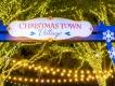 Busch Gardens Christmas Town A sign saying "Christmas Town Village" on an archway in front of trees lit with strings of lights