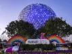 Festival of the Arts at EPCOT Spaceship Earth lit up in the early evening. In front of it is a large paint tube and a Festival of the Arts sign next to two rainbows