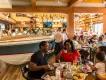 The Boathouse People eating in a full restaurant dining room sat at tables surrounding a large speedboat