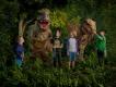 Dino Mania at Dubai Parks and Resorts 4 children standing in some foliage with two dinosaur animatronics