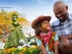 EPCOT International Flower & Garden Festival A young boy dressed as a cowboy smiling up at his dad. They are both sat in front of a topiary shaped like Bo Peep from Toy Story