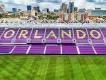 Orlando City Stadium One side of a football stadium's seats with a cityscape in the background. The seats are purple with detailing that spells out "Orlando"