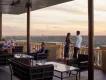 Capa in the Four Seasons hotel Terrace with brown chairs and glass tables on, there are two groups of two people sat to the left of the image and a couple stood up overlooking the view of the terrace.