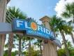 Florida welcomes you sign A blue sign with white text which says 'Florida Welcomes You' with palm trees in the background.