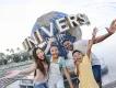 Universal Studios Florida A family of four stood in front of a big circular statue of the globe with white capital letters on spelling UNIVERSAL. The family are smiling and have their arms spread wide. There is a couple with one daughter and one son.