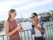 Universal Studios Florida food Two women stood eating snacks in Universal Studios Florida, with a lake and rollercoasters in the background. One is eating a long churro and the other is eating a pretzel.