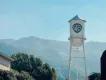 Warner Bros. Studio White water tower with blue shield shaped logo with letters WB on. In the background there is a large tree and big mountains with a blue sky overhead.