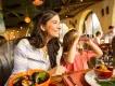 A woman and child dining in the Animal Kingdom Lodge, the mother is smiling looking off camera through a window and the little girl is also smiling looking in the same direction with binoculars held against her eyes. The mother has a bowl of seafood in front of her whereas the girl has a plate with chicken curry, rice and green beans.