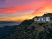 Large mountains surrounding a city. There is a large sign with capital letters spelling out "HOLLYWOOD". In the background there is a sunset with pink and orange colouring.