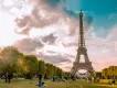 The Eiffel Tower Large triangular steel structure standing tall behind park lined with trees.
