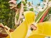 Birds eye view of man dropping down the top of a yellow vertical drop slide, beside there is a red which is smaller. There are pools below and walkways with people queueing for smaller waterslides.