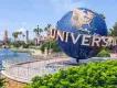 Universal Studios Florida entrance Large circular sign shaped as the globe with white letters in bold curving around it spelling out "UNIVERSAL". In the background there is a lake, palm trees and a tall sign made from rock which says Islands of Adventure.