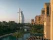 Burj Al Arab Beige buildings with a river beside them and some trees. It is sunset and the view shows the Burj Al Arab, a ship sail shaped building.