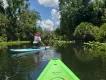 The Paddling Center A person sat on a green kayak and a young person on paddle board in front kneeling by the water.