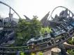 Jurassic World VelociCoaster Grey rollercoaster on grey track with twisting track around trees and grey rocks. The coaster is empty.