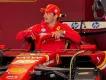 Carlos Sainz in Ferrari Famous Ferrari driver hopping in his famous Formula 1 Ferrari car in the garage with red walls. He is wearing a red cap which is branded and is wearing a red hoodie with the Ferrari logo on it.