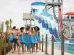 Island H2O Water Park Group of six young adults holding blue mats walking away from large blue water slides. There are six identical slides with a small drop which leads to a bigger drop.