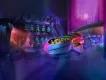 Justice League: Warworld Attacks Two rows of guests sat in ride vehicle shaped like futuristic car in a dark building. They're wearing 3D goggles and in the background the wall has many test tubes lined up with green substances in them.