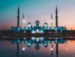 Abu Dhabi A beautiful religious temple in Abu Dhabi located overlooking a lake. The sun is setting with a pink and blue hue in the sky and the temple is perfectly reflected in the lake. It is a white building with three white domes and four big pillars sticking out.