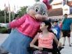 Give Kids The World A young girl in an electric wheelchair looking up at a large bunny dressed in a pink jacket and pink bow.