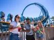SeaWorld Seven Seas Food Festival Three people stood in front of Pipeline, a standing up rollercoaster, holding small plates and cups full of red cocktails.